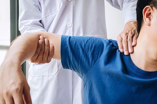 Doctor physiotherapist assisting a male patient while giving exercising treatment massaging the shoulder of patient in a physio room, rehabilitation physiotherapy concept.
